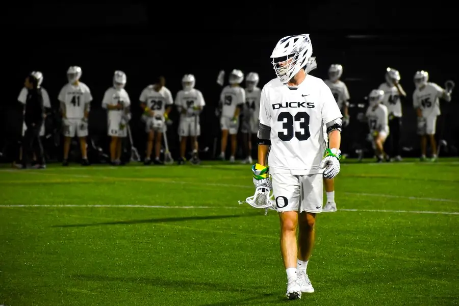 Oregon Ducks lacrosse player with teammates on the sideline