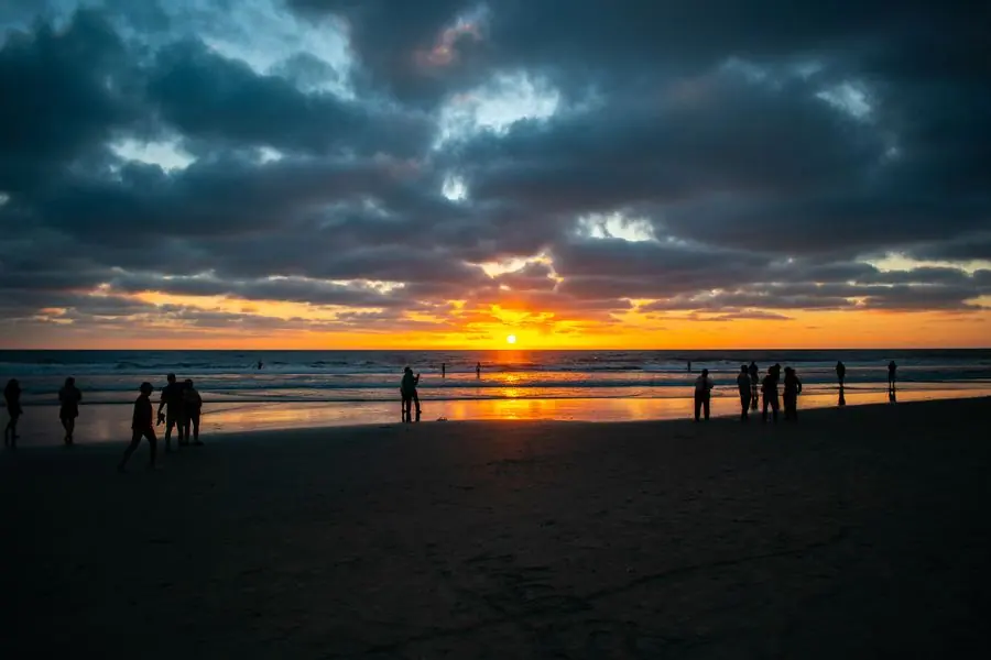 Silhouettes of beachgoers watching a fiery sunset over the ocean