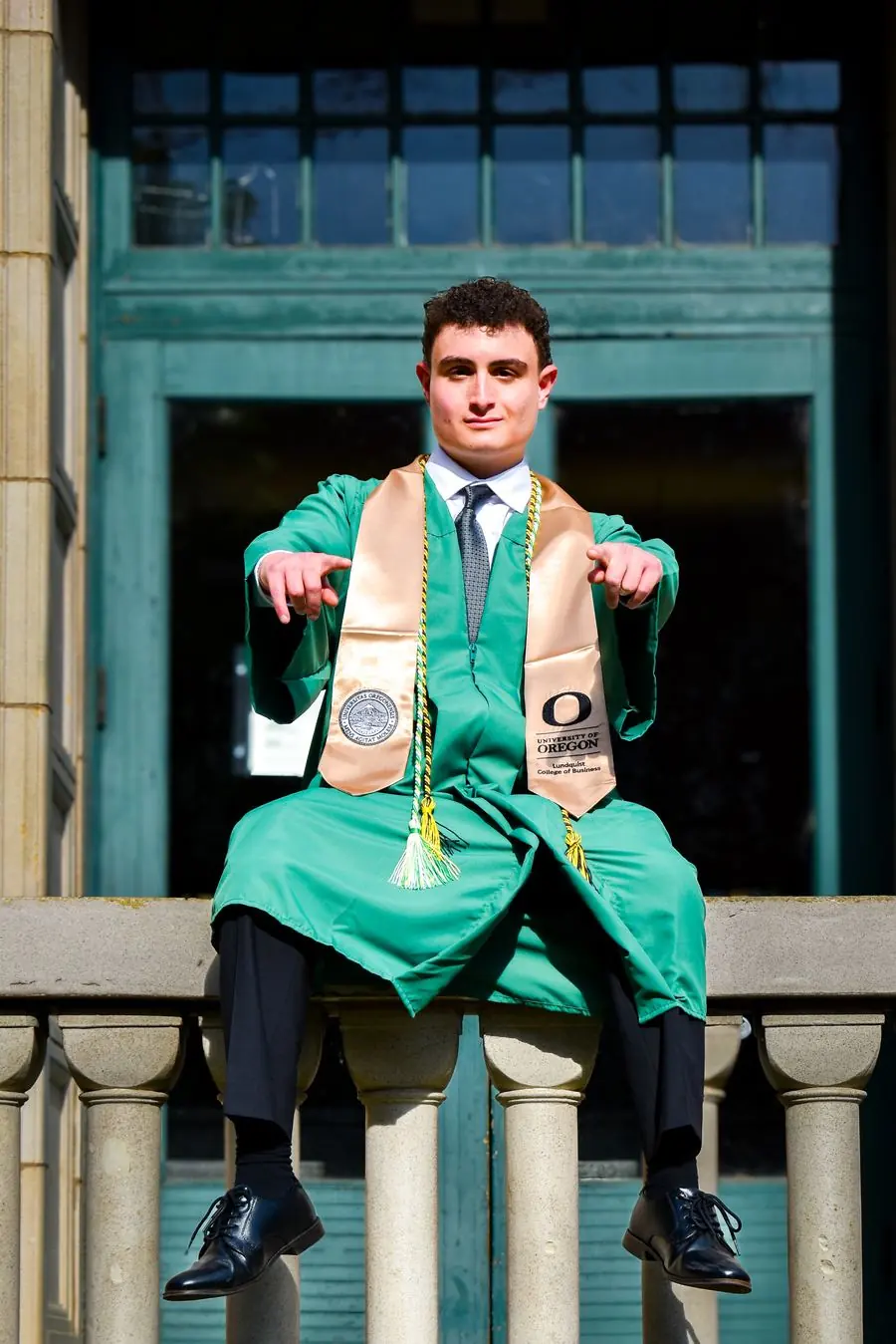 University of Oregon graduate sitting on a stone balustrade, giving a playful pose