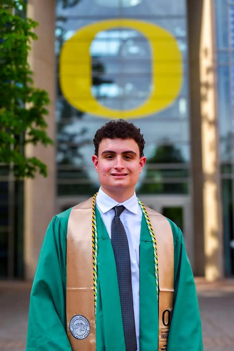 University of Oregon graduate smiling in front of the giant O sign