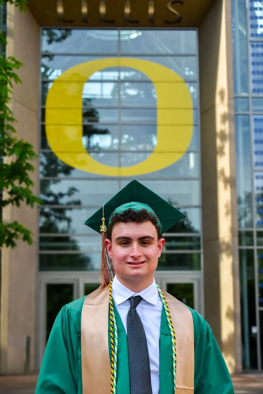 Graduate in cap and gown outside Lillis Hall with the O sign behind him
