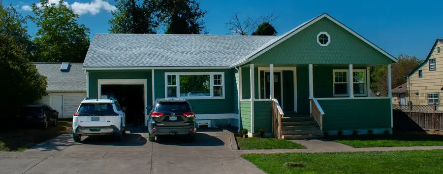 Green craftsman home with a two-car driveway and covered porch