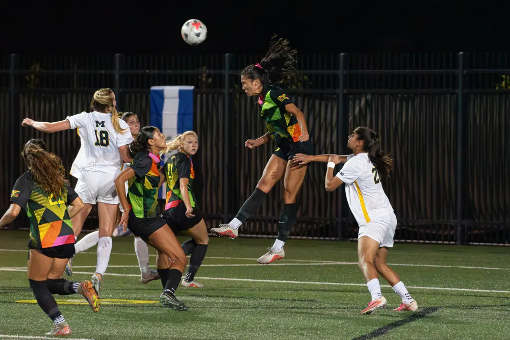 Oregon women's soccer player rising for a header against Michigan at night
