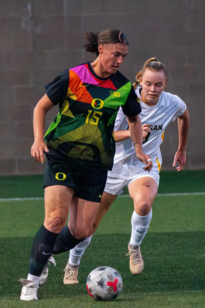Oregon women's soccer player No. 15 dribbling ahead of a Michigan defender