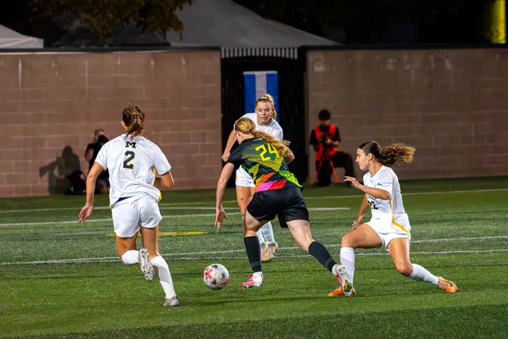 Oregon women's soccer player No. 24 cutting between Michigan defenders