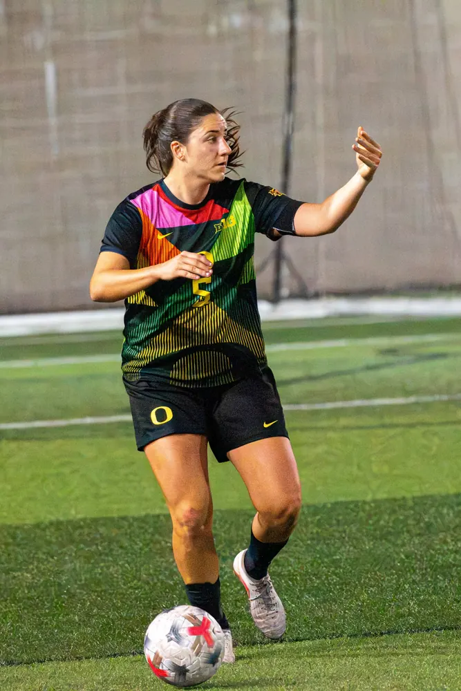 Oregon women's soccer player No. 5 directing teammates while dribbling