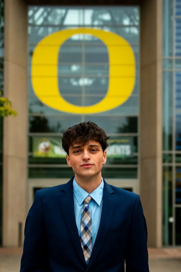 Headshot of a man in a navy suit and plaid tie beneath the University of Oregon O