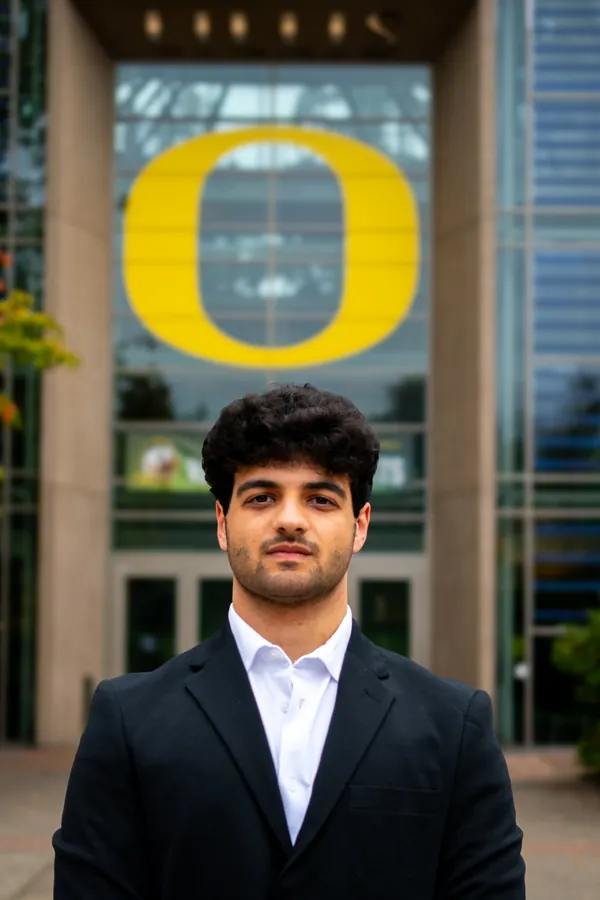 Headshot of a man in a black blazer and white shirt beneath the University of Oregon O